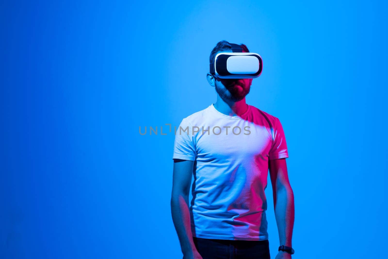Bearded young man in a white t-shirt wearing virtual reality goggles in modern coworking studio. by vovsht