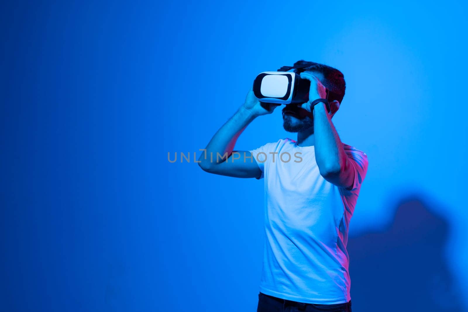 Portrait of young man with 3D virtual reality glasses enjoys his trip in an adventurous world in neon light. Concept of connection technology with science, augmented reality