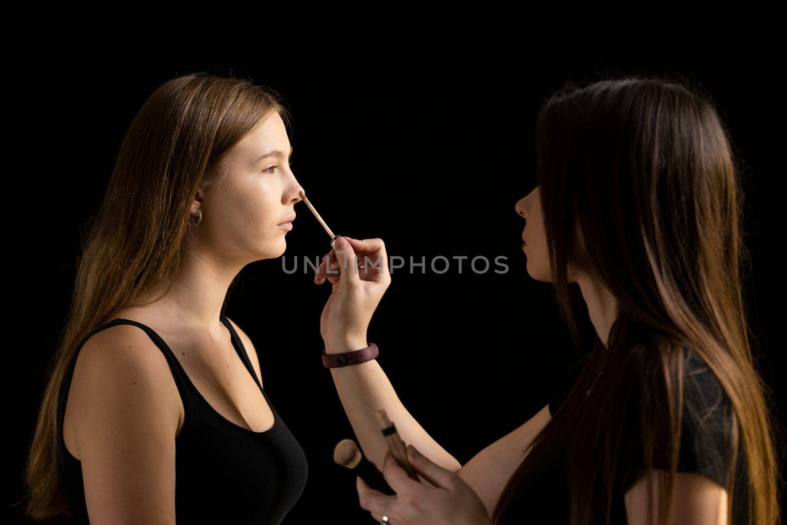 Makeup artist applying liquid tonal foundation on the face of the woman in make up room. Professional make-up artist working with brush on model face