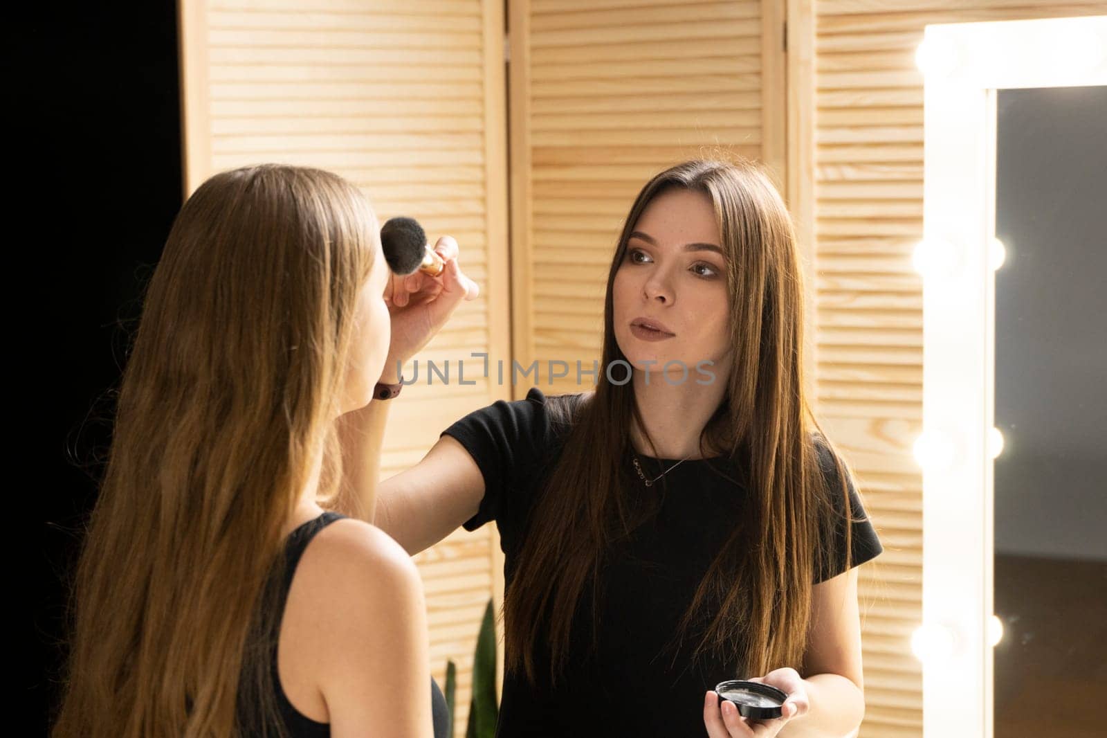 Make-up artist applying powder with a brush on model's cheeks. Professional make-up