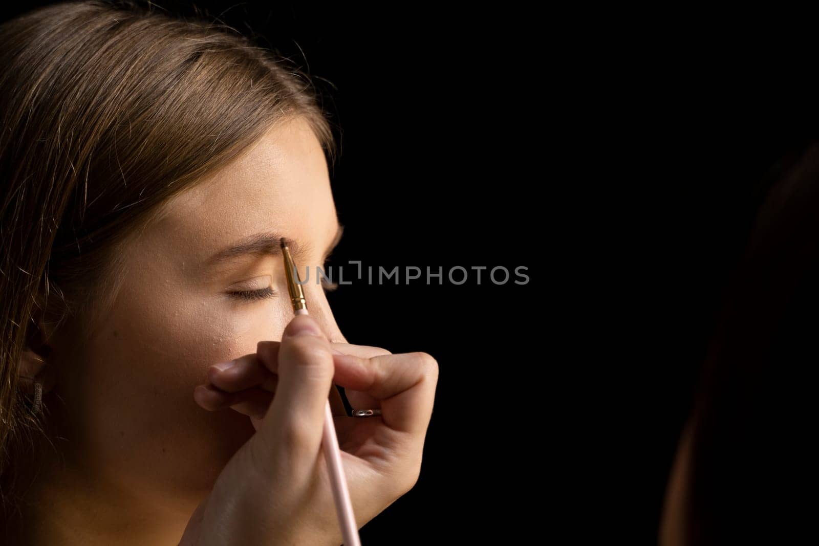 Makeup artist doing a eyebrows makeup on a beautiful woman face. Hand of make-up master is painting eyebrow of young beauty model girl. Make up in process