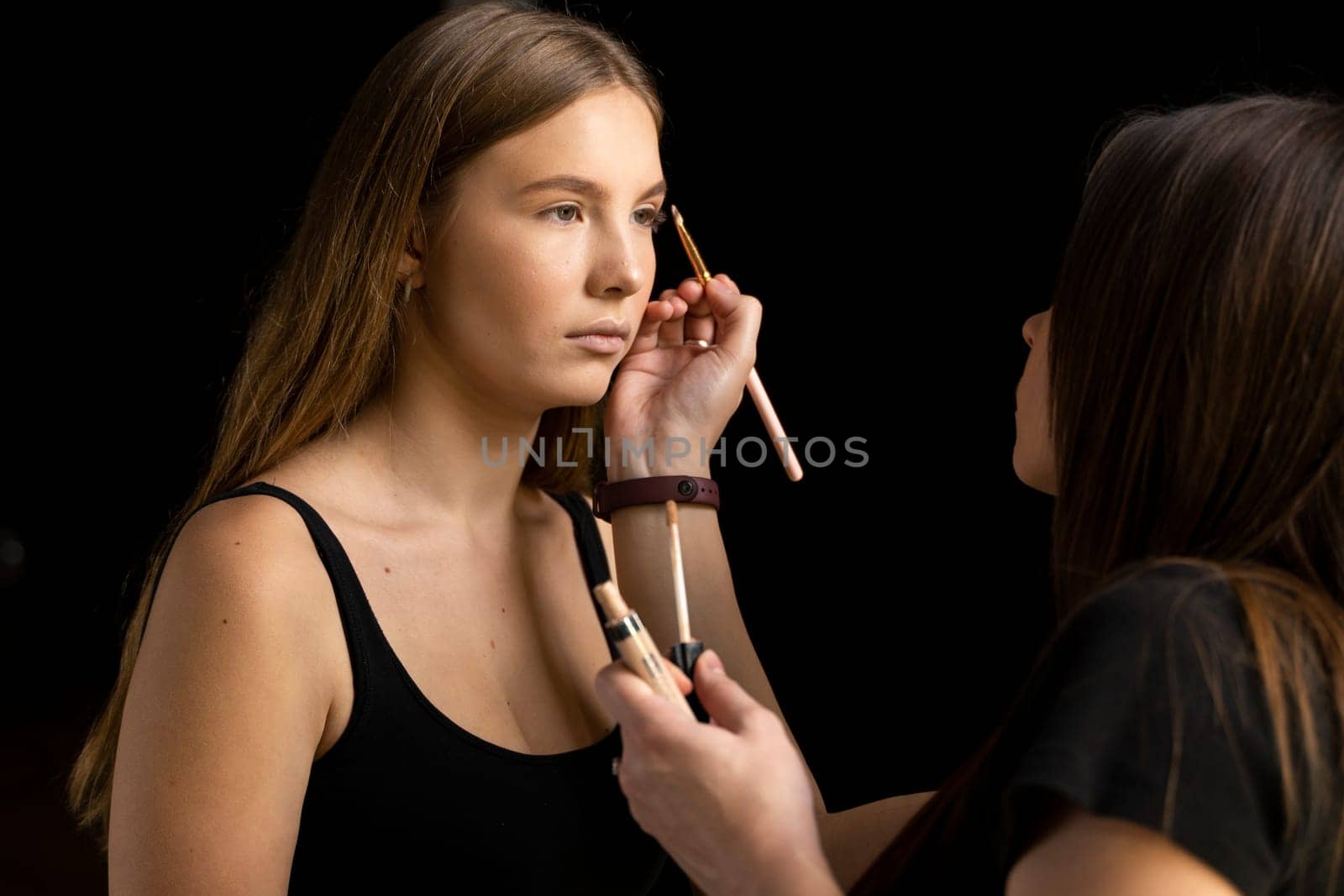 Makeup artist doing a eyebrows makeup on a beautiful woman face. Hand of make-up master is painting eyebrow of young beauty model girl. Make up in process. by vovsht