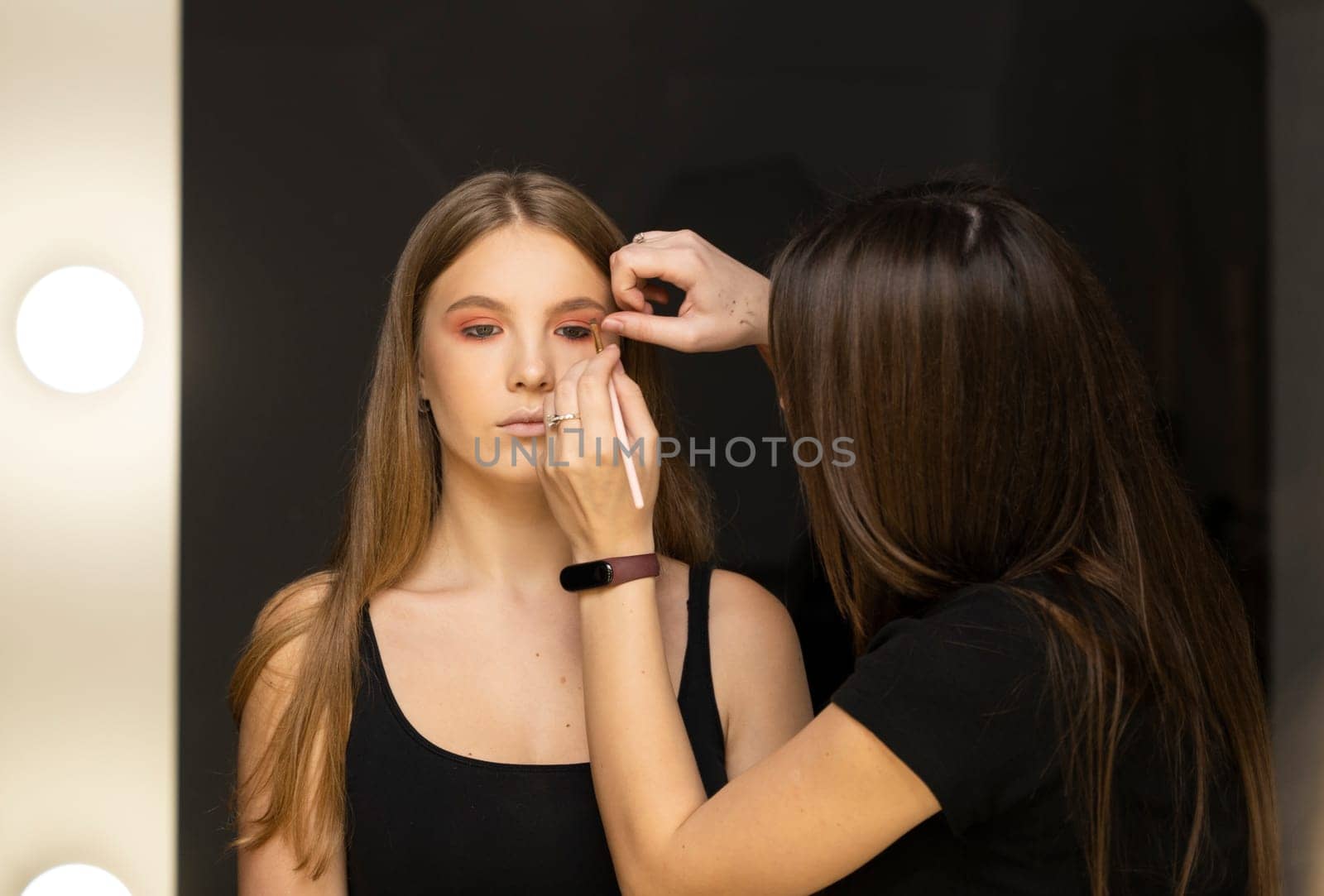 Makeup artist applying liquid tonal foundation on the face of the woman in make up room. by vovsht