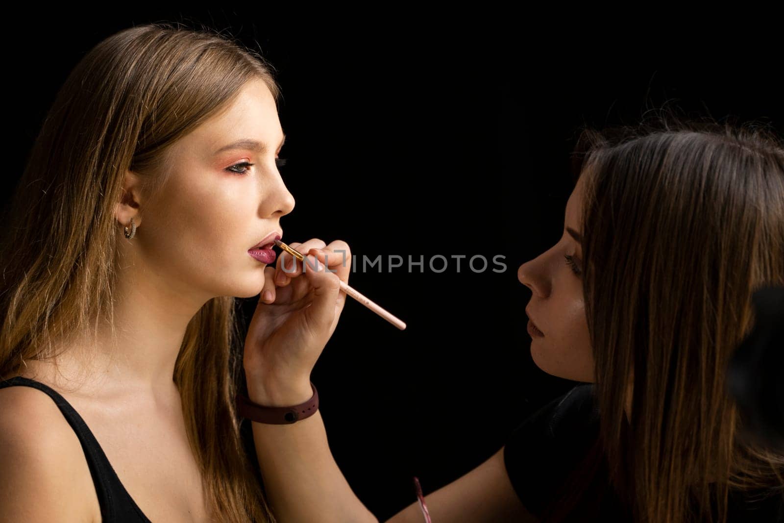 Makeup artist applies red lipstick on a beautiful young woman model face. Hand of make-up master, painting lips of young beauty model girl. Make up in process