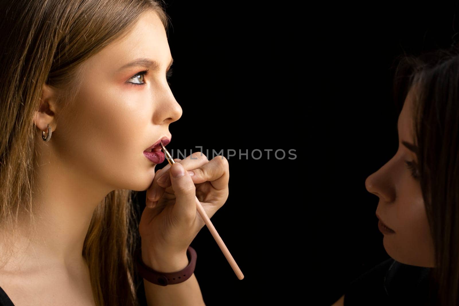 Professional make-up artist applying bright red lipstick on beautiful girl using special lip brush. by vovsht