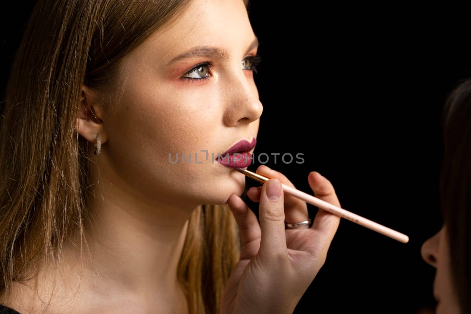 Makeup artist applies red lipstick on a beautiful woman face. Hand of make-up master, painting lips of young beauty model girl. Make up in process