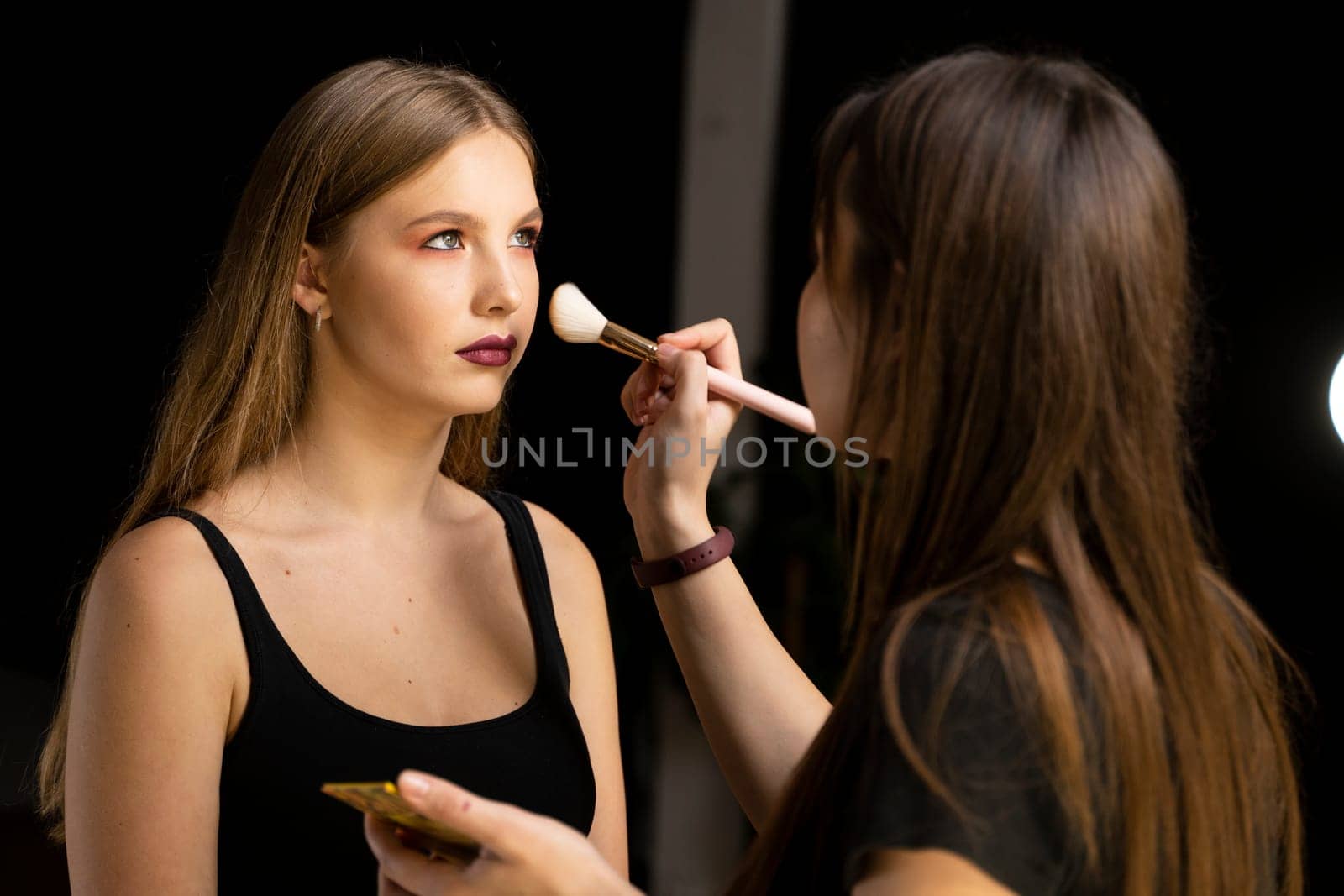 Process of making makeup. Make-up artist working with brush on model face. Portrait of young blonde woman in beauty saloon interior. Applying tone to skin