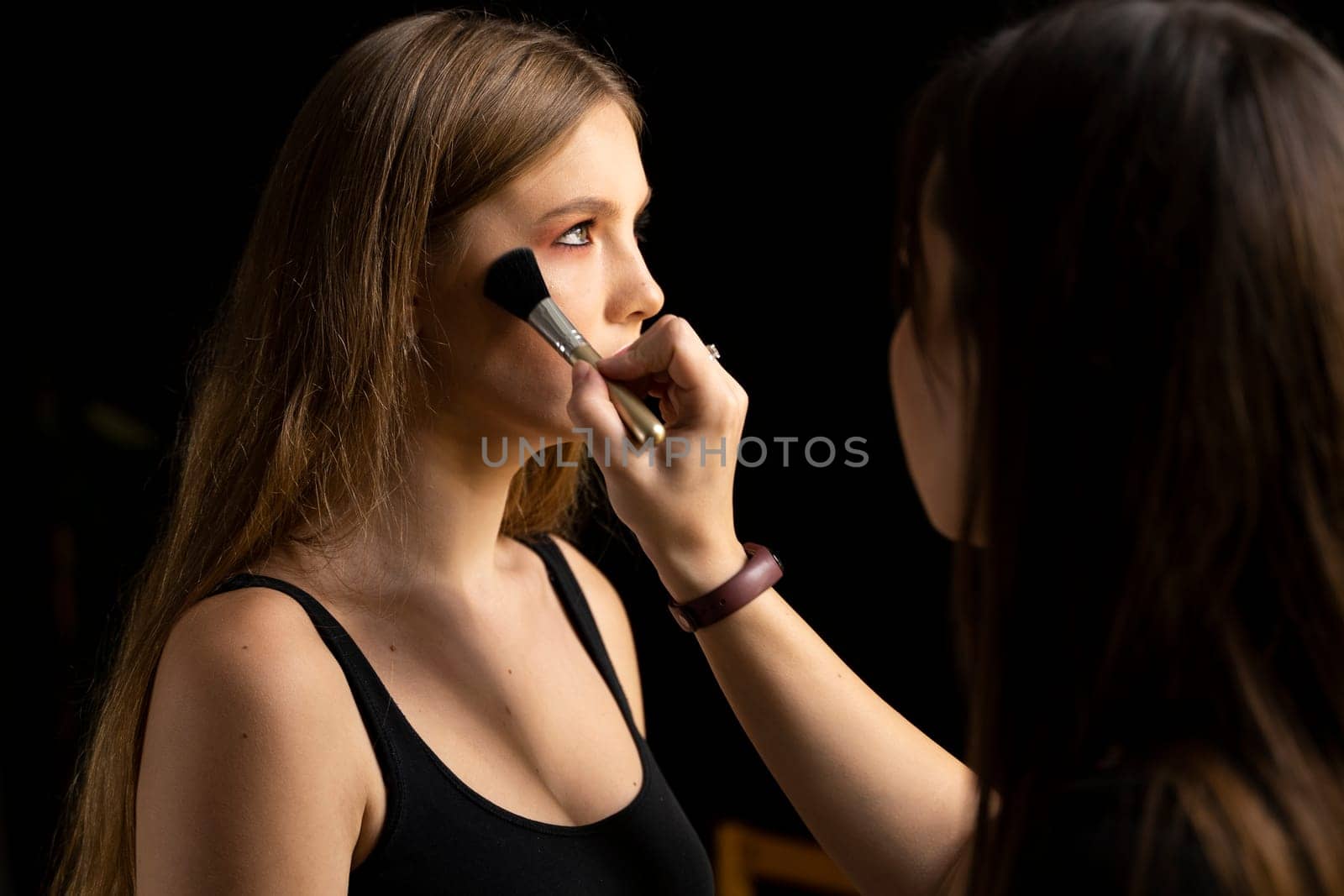 Close up face of beautiful young woman getting powder on her cheek with a brush. Professional makeup artist. by vovsht