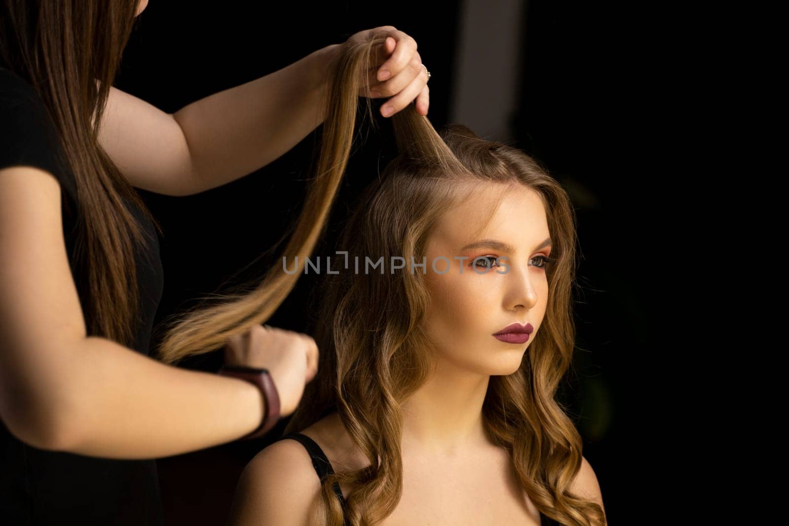 Professional hair stylist prepares woman makes curls hairstyle in a beauty salon. Long light brown natural hair