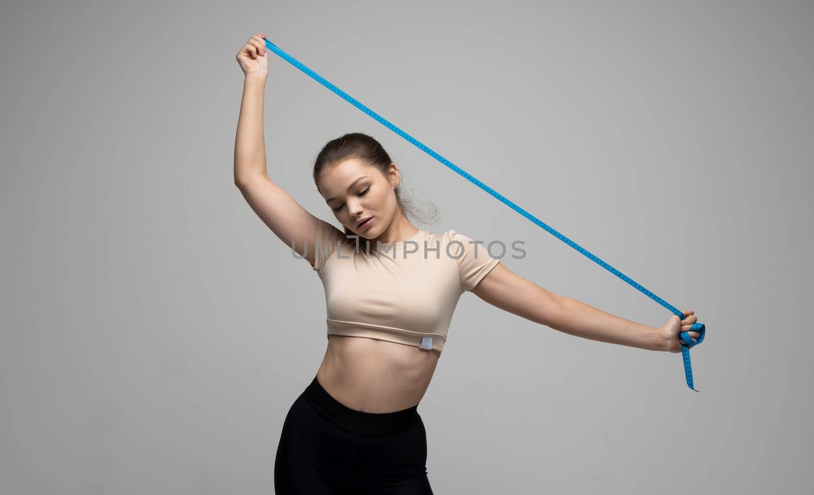 Attractive brunette woman in sportswear holding a blue measuring tape. Weight loss and diet concepts. Health care and healthy nutrition. Perfect slim body. by vovsht