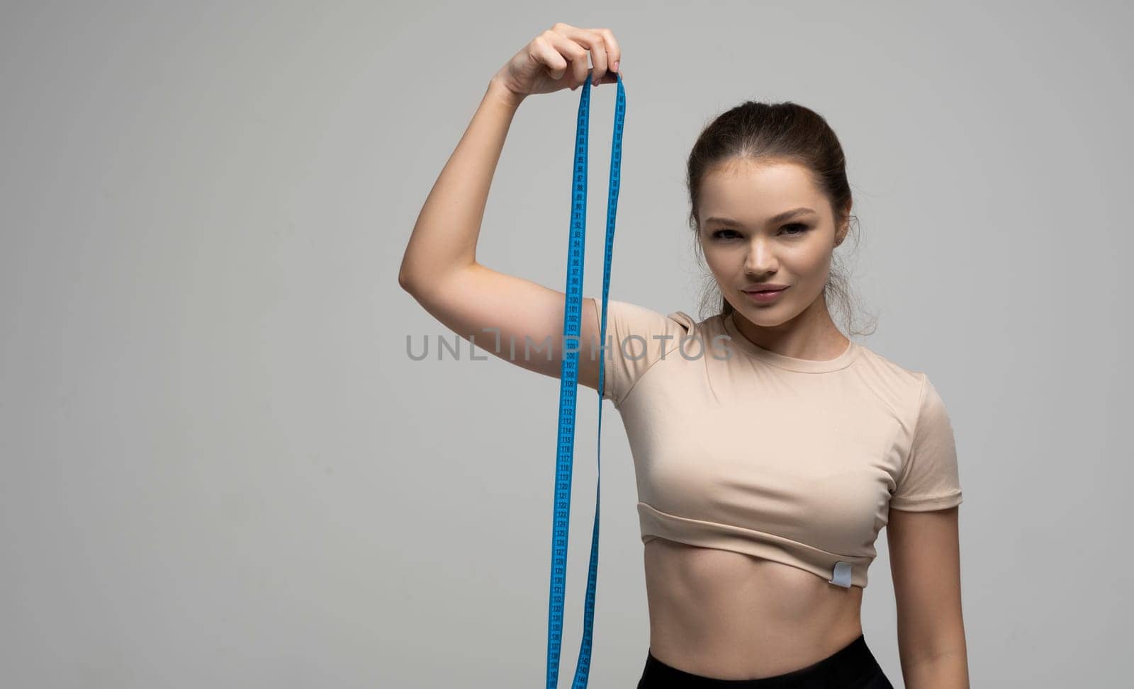 Brunette woman in a sport wear with a blue measuremt tape after her body measurements on white background. Healthy lifestyles concept