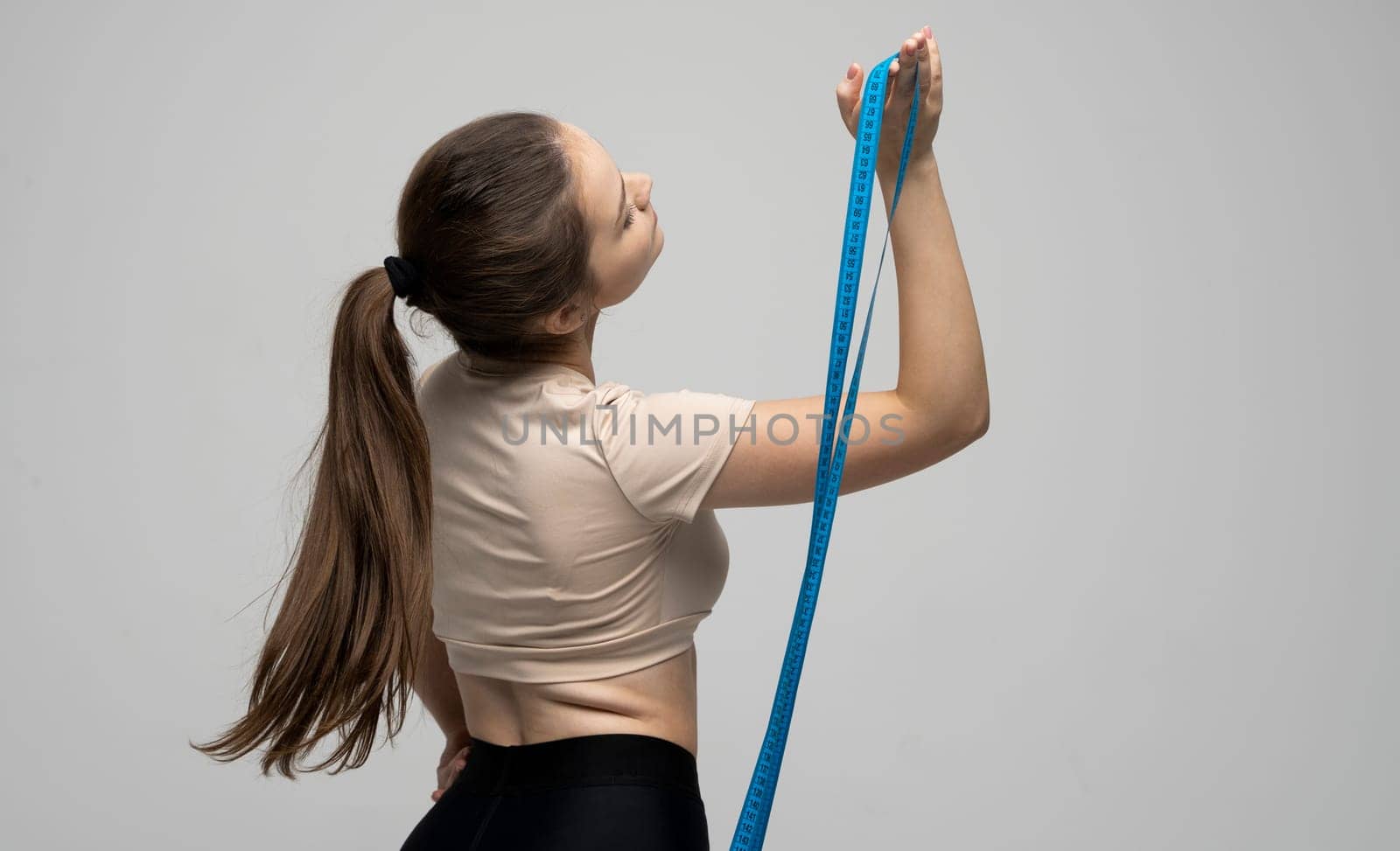 Back of attractive brunette woman in sportswear holding a blue measuring tape. Weight loss and diet concepts. Health care and healthy nutrition. Perfect slim body. by vovsht