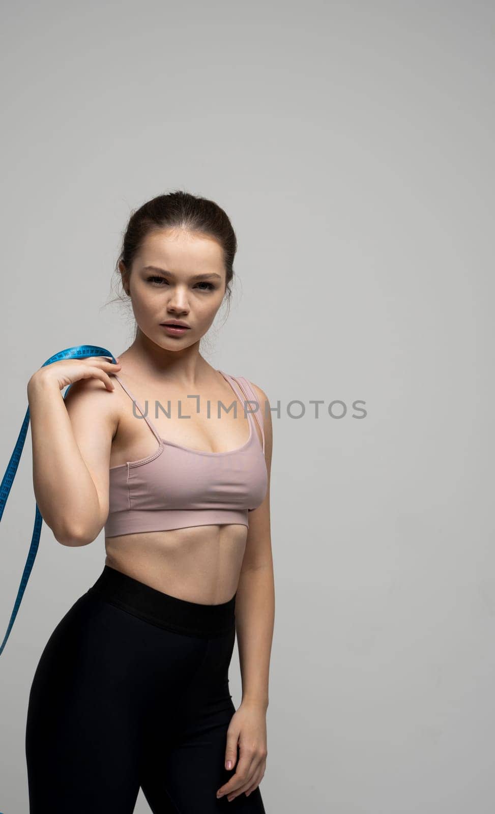 Portrait of brunette woman in sportswear holding a blue measuring tape. Weight loss and diet concepts. Health care and healthy nutrition. Perfect slim body
