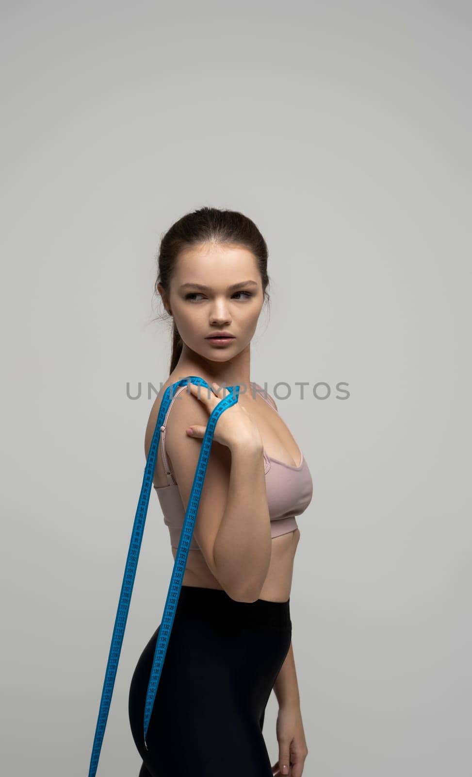 Woman with a perfect shape of healhy body standing with measuremt tape and happy with result of exercise training on white studio background. Weight loss and healthy lifestyles concept