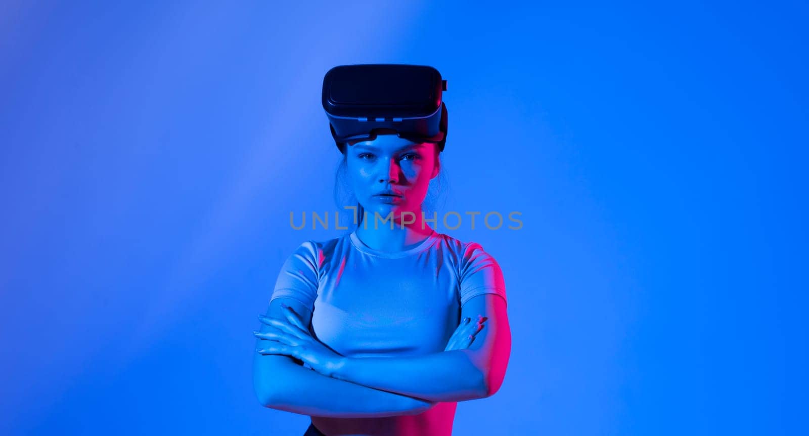 Portrait of young brunette woman gamer with virtual reality headset on a head looks straight in a camera with a hands crossed on a breasts. by vovsht
