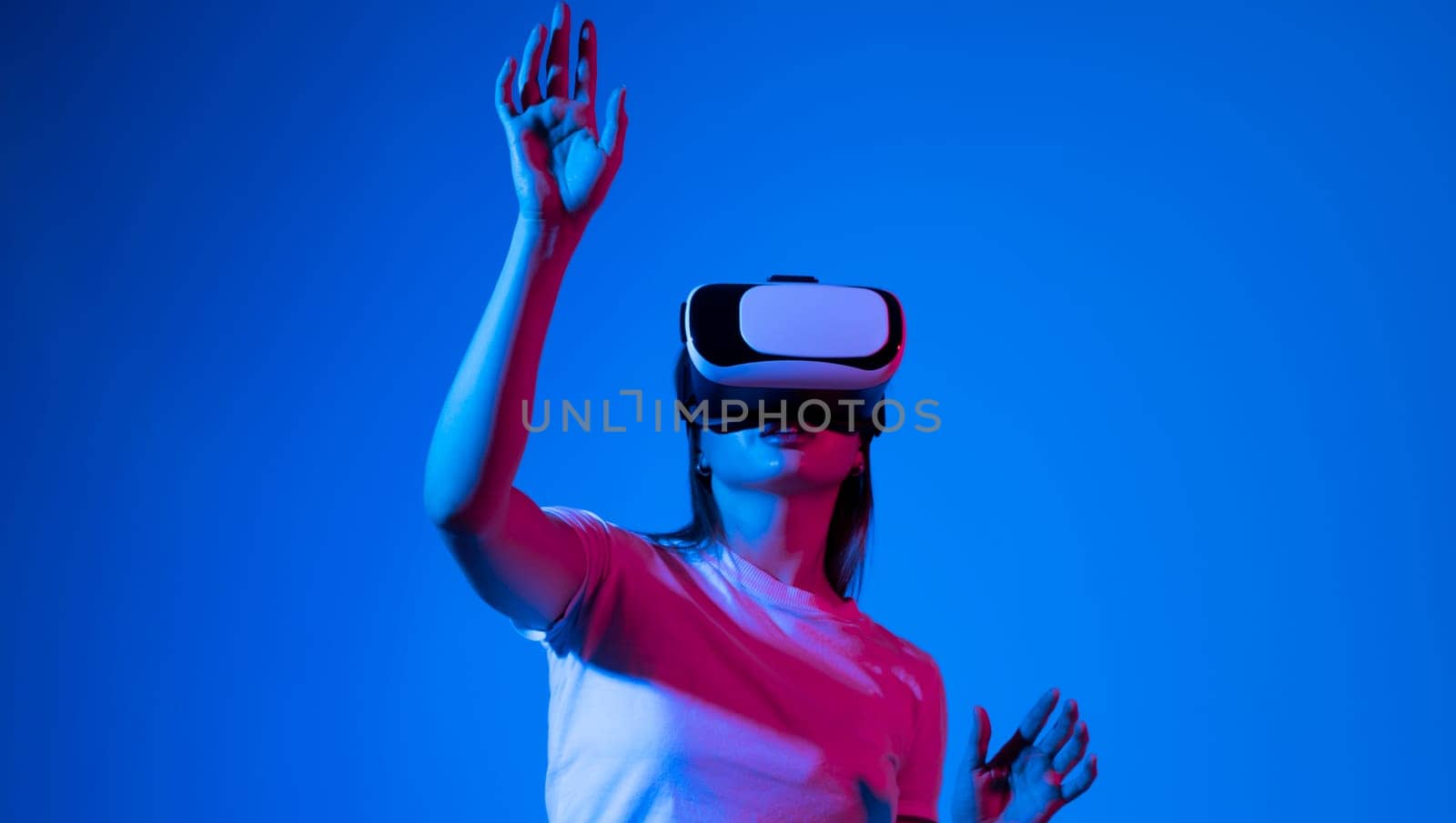 Brunette woman in virtual reality headset playing a video games with a friend's and gesturing with a hands in a neon light. Future gaming concept