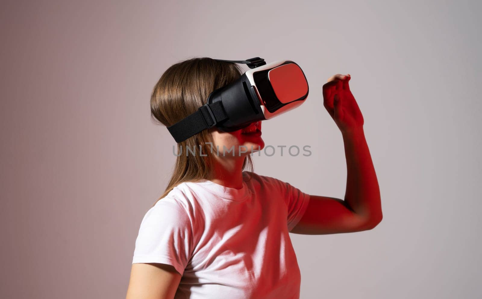 Woman gamer in white t-shirt wearing virtual reality headset and playing a video games with a friend's and gesturing with a hands in a red light. Future gaming concept