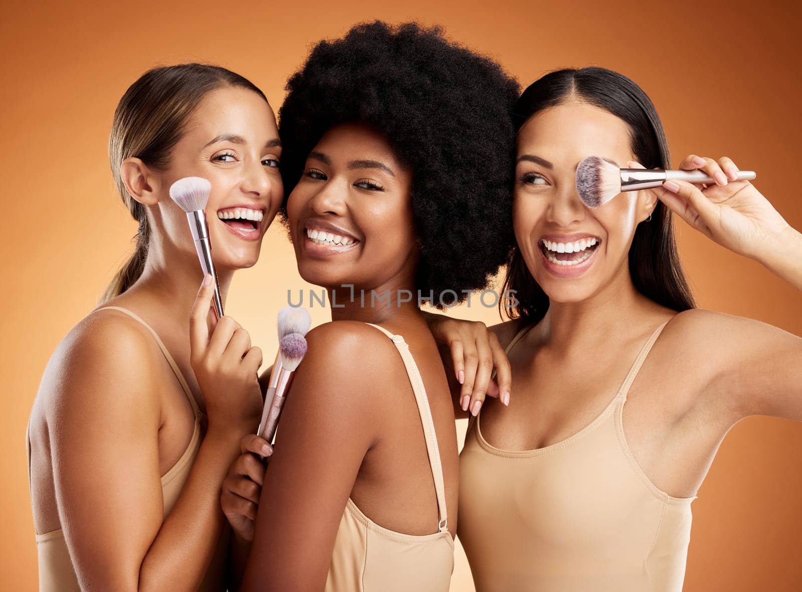 Makeup, beauty and women with brush for cosmetics against a brown mockup studio background. Face portrait of happy, smile and young model group with product for facial foundation and skincare by YuriArcurs