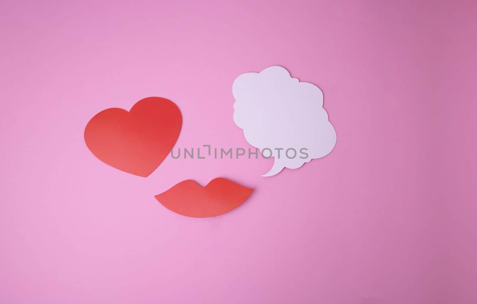 On a pink background paper red lips and a heart and a white cloud for words.