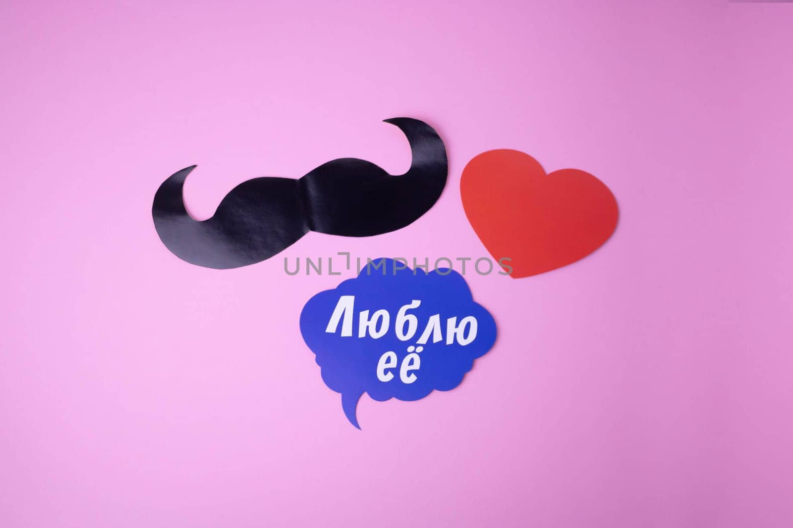 On a pink paper background, a black mustache, a red heart, a blue cloud with the words I love her .