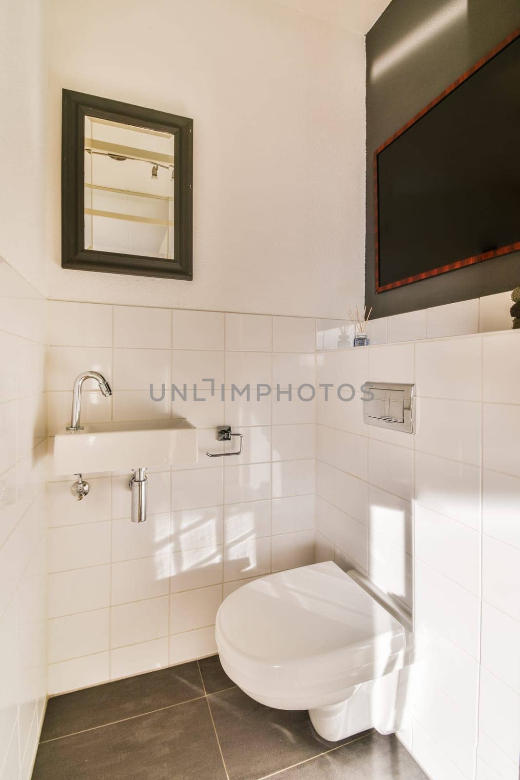 a small bathroom with a toilet and tv above the toilet bowl, in a white tiled wall behind it is a black framed mirror