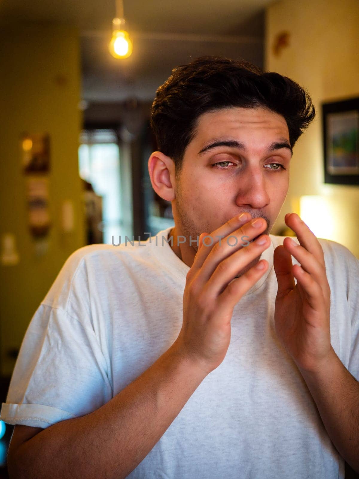 Young man about to sneeze, with hands in front of his nose, standing in living room at home