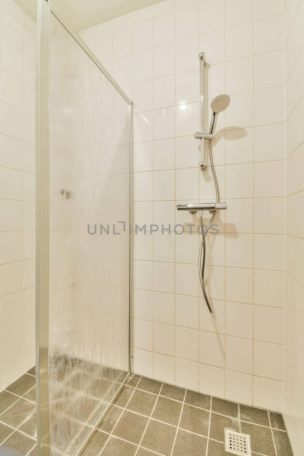 a shower stall with water coming from the shower head and hand held up to it's side, in a white tiled bathroom