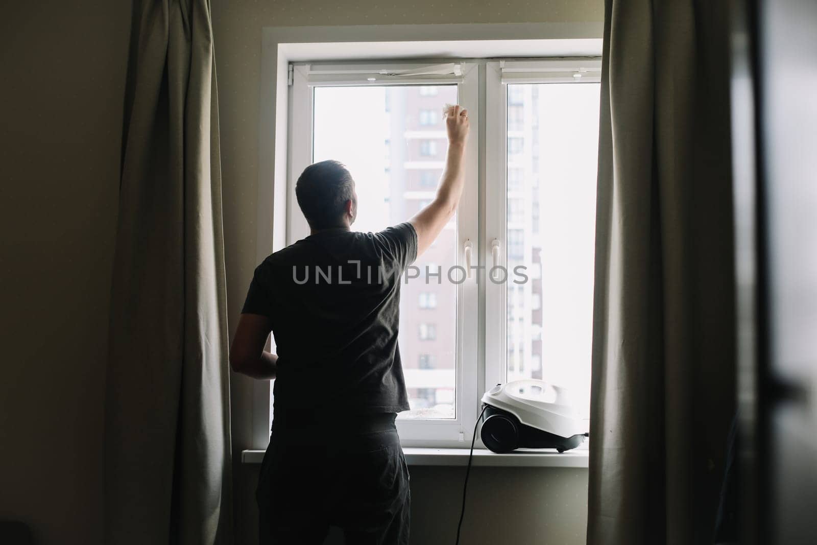 Man washing and cleaning window at home. Housework and housekeeping, home hygiene by paralisart