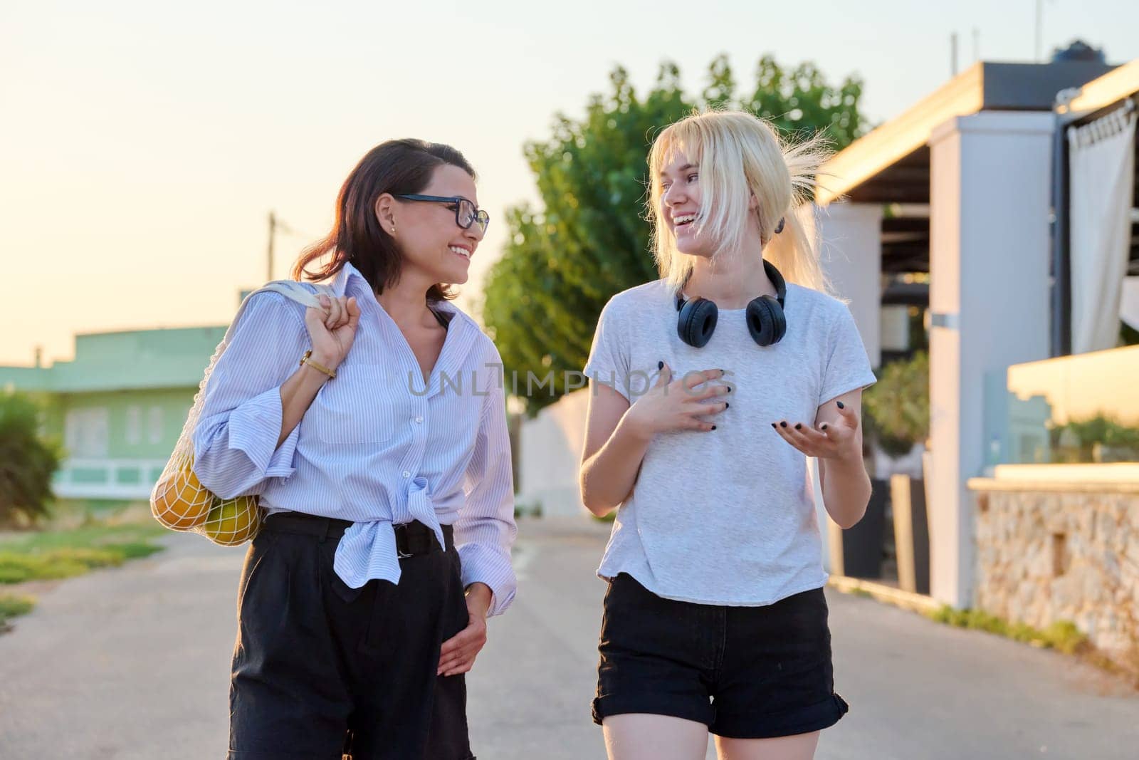 Outdoor portrait of happy mom and teenage daughter walking together by VH-studio