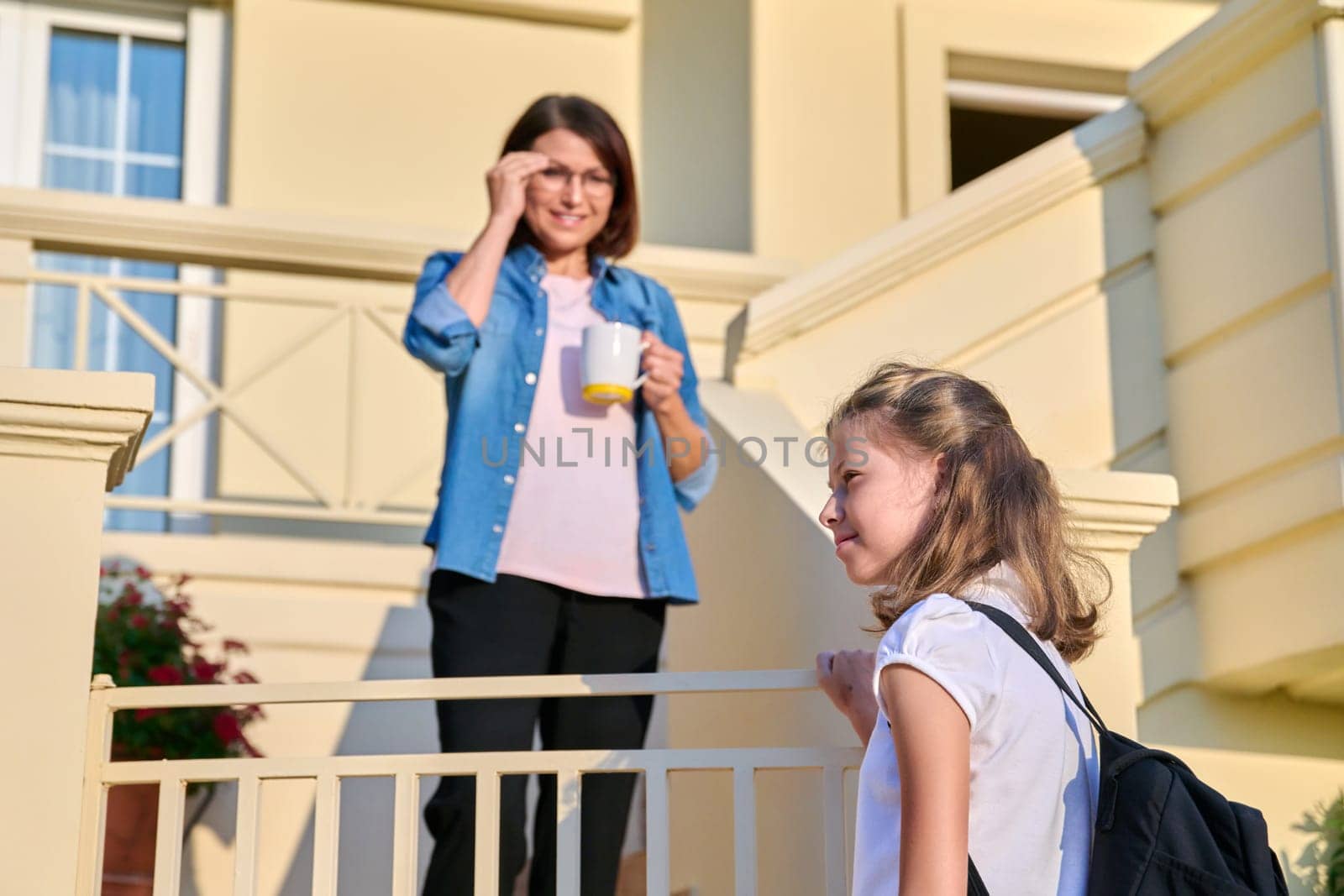 Girl student with a backpack on the porch of the house with her mother. by VH-studio