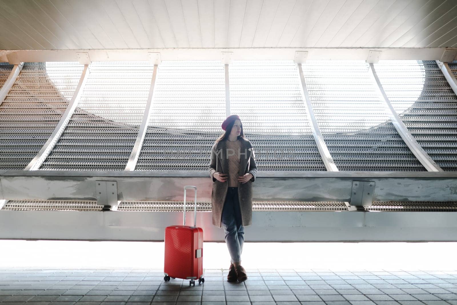 Young female traveler walking with a red suitcase at the modern airport. Concept of an urban transportation and travel.