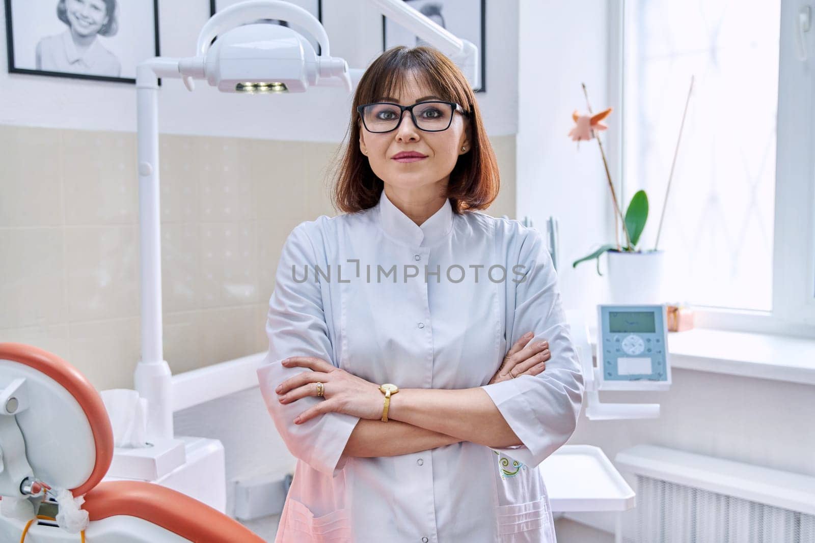 Portrait of smiling mature female dentist looking at camera in office. Confident doctor with crossed arms in clinic. Dentistry, medicine, health care, profession, stomatology concept