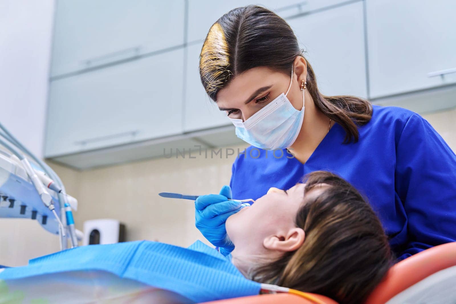 Doctor dentist treats teeth to a young teenage female patient. Real process of treatment, dental care, orthodontics, therapy, health care, dentistry concept