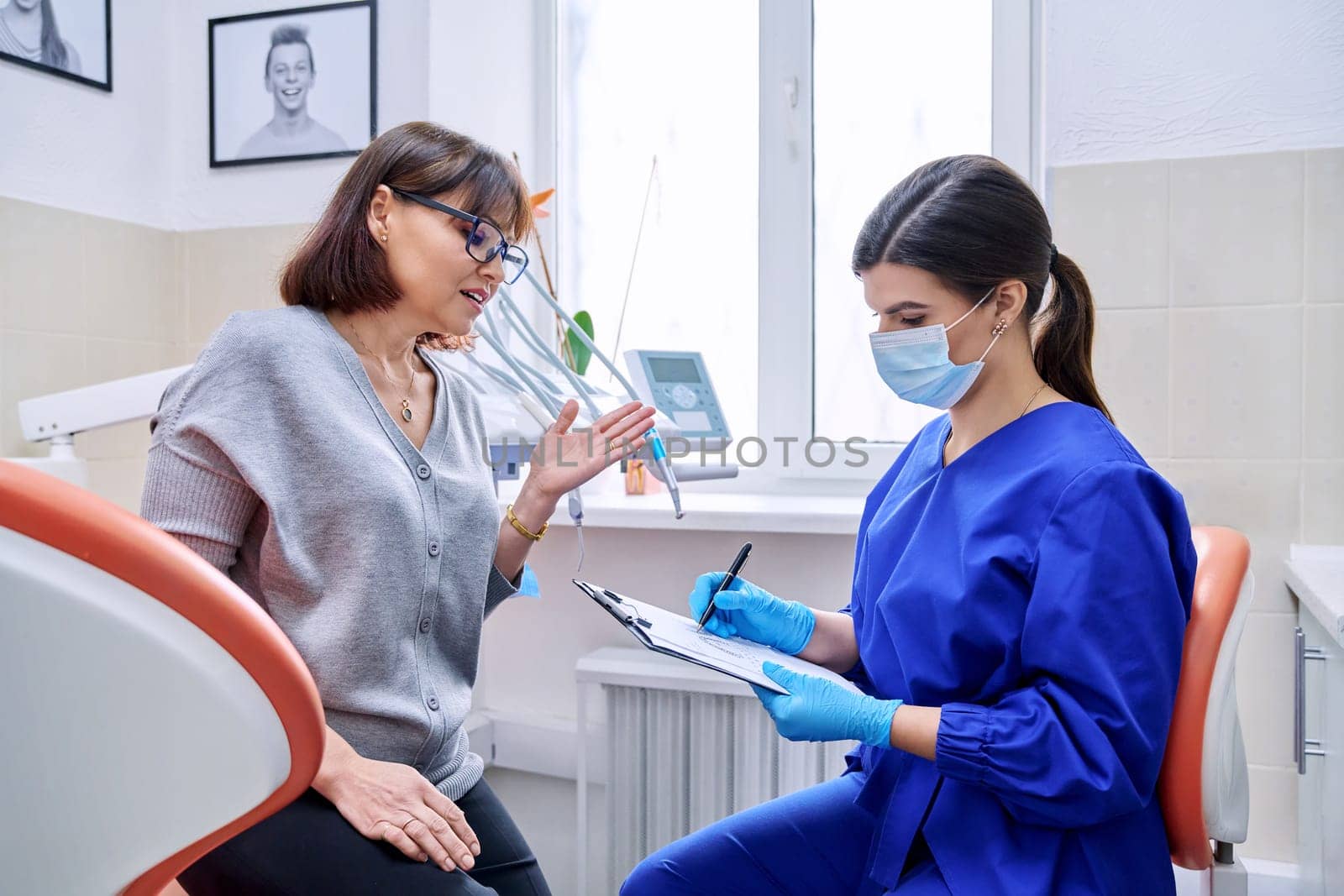 Dental office visit, female patient talking to doctor, dentist making notes by VH-studio