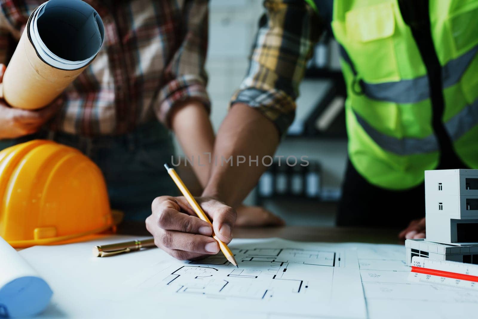 Engineers are consulting the team to design an architectural structure for clients with blueprints and building models to work at office by Manastrong