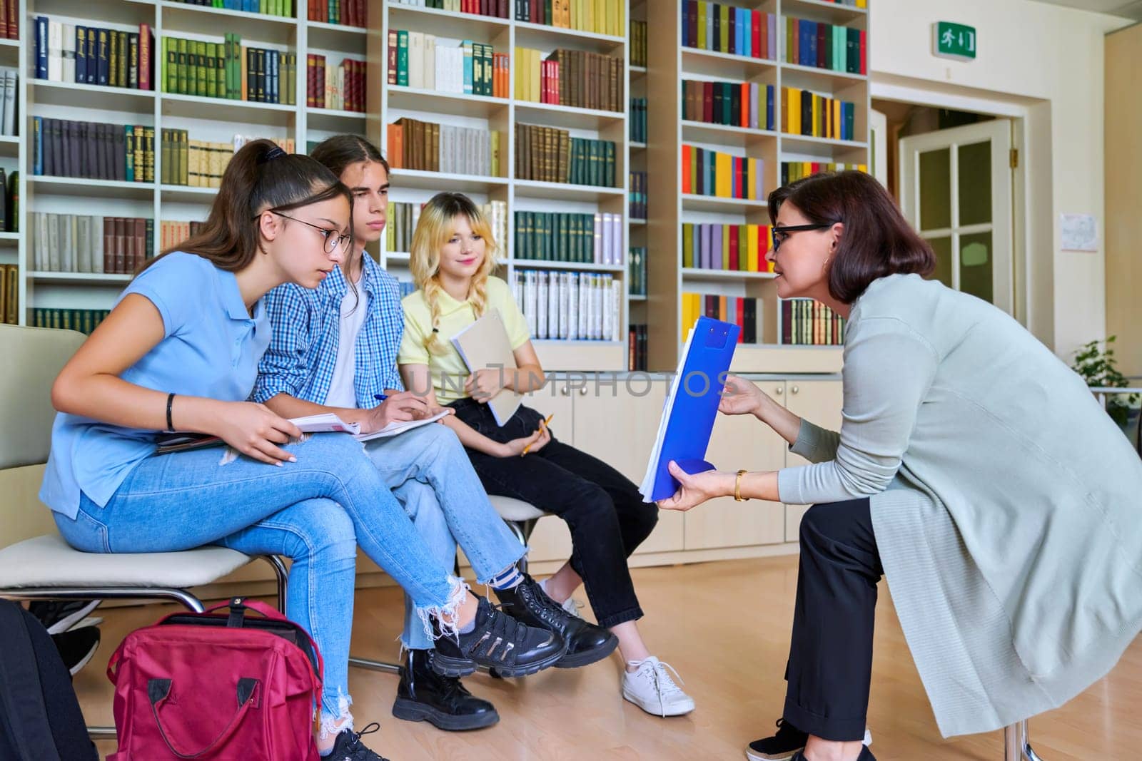 Group of teenage students studying in library class with female teacher mentor by VH-studio