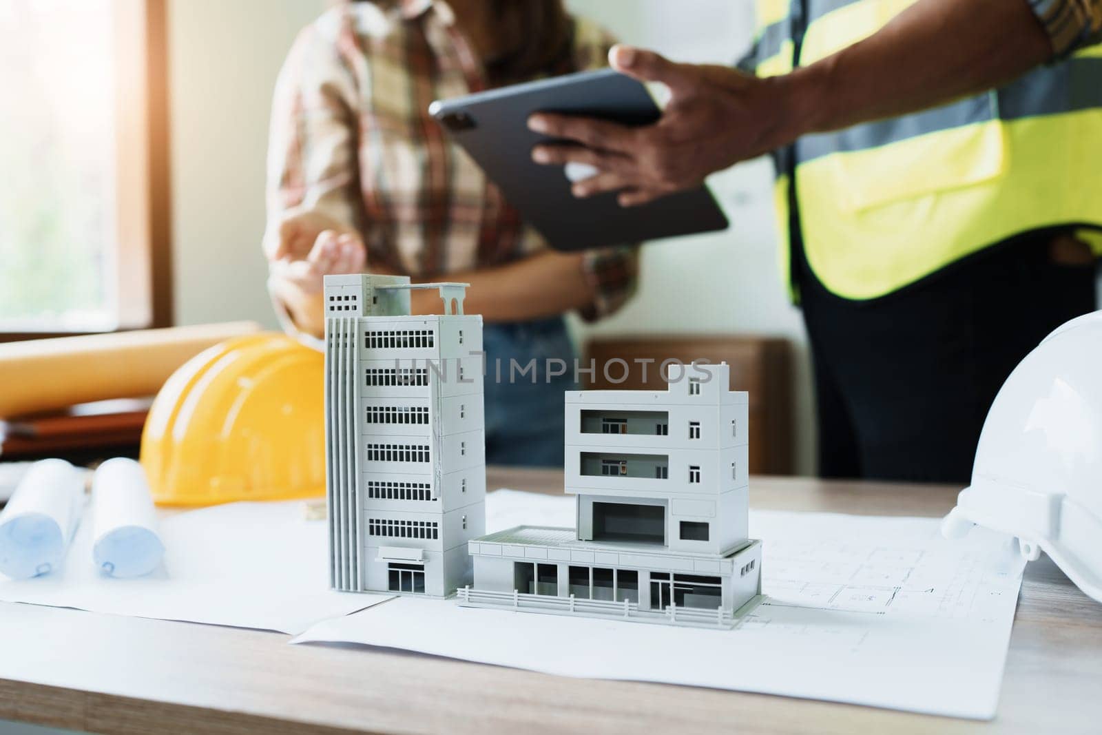 Engineers are consulting the team to design an architectural structure for clients with blueprints and building models to work at office by Manastrong