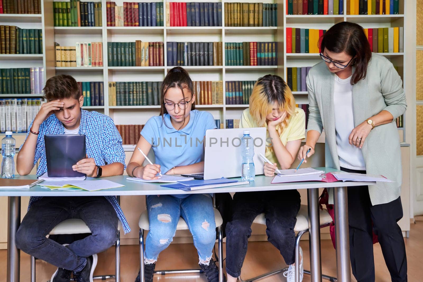 Group of teenage students studying in library class with female teacher mentor by VH-studio
