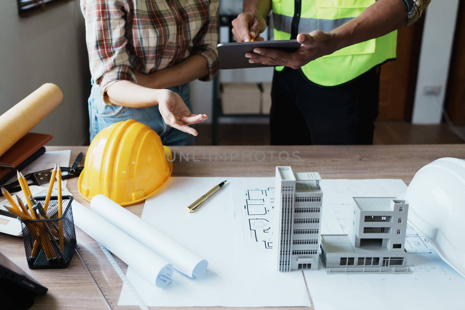 Engineers are consulting the team to design an architectural structure for clients with blueprints and building models to work at office by Manastrong