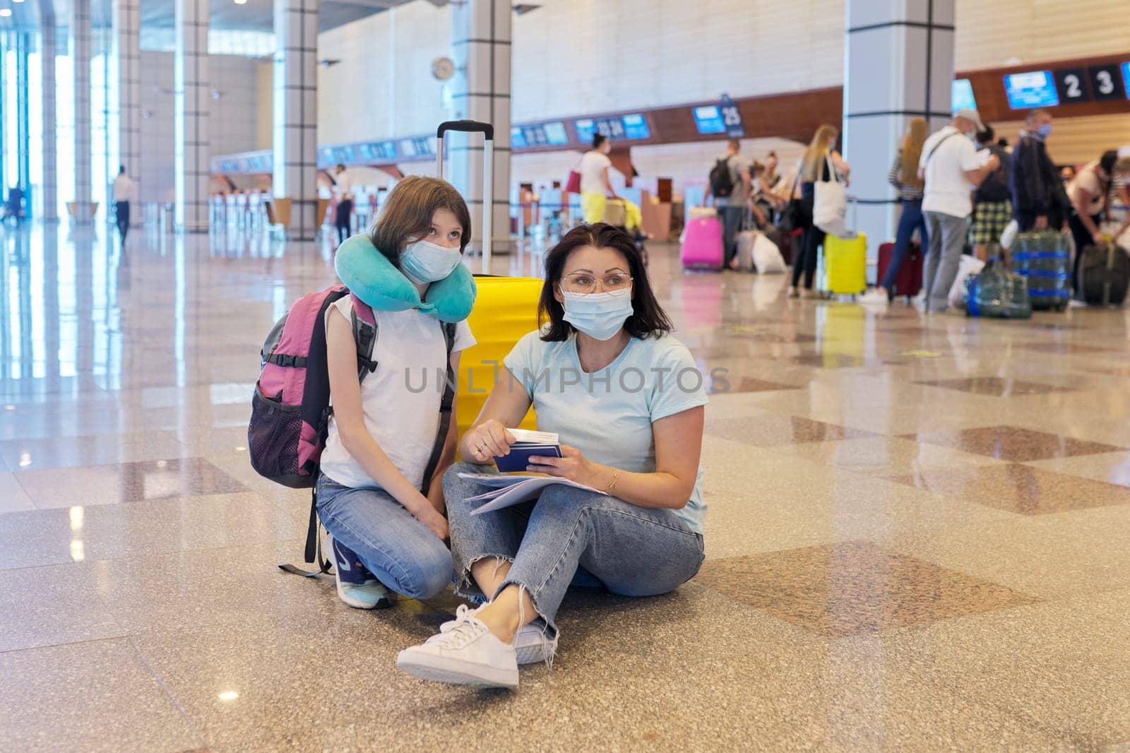 Mother and daughter child in protective medical masks at the airport with luggage by VH-studio