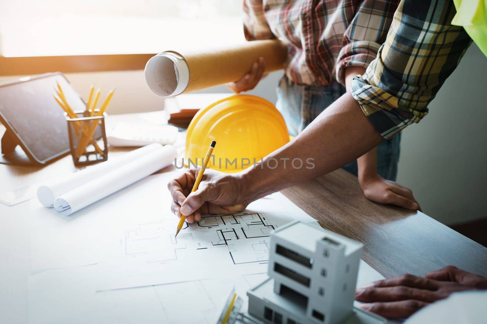 Engineers are consulting the team to design an architectural structure for clients with blueprints and building models to work at office by Manastrong