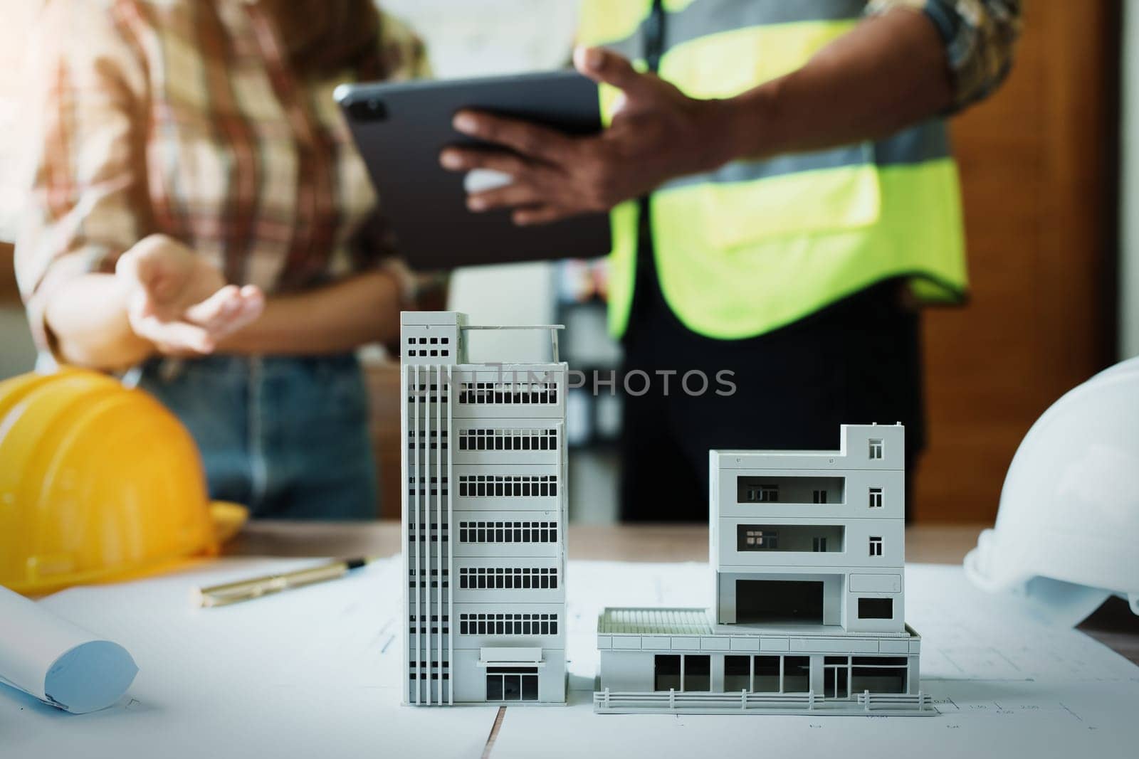 Engineers are consulting the team to design an architectural structure for clients with blueprints and building models to work at office by Manastrong