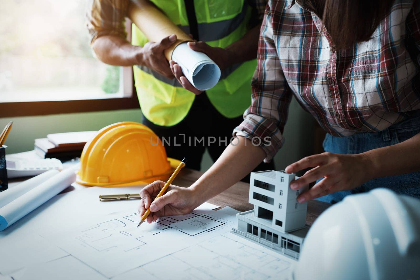 Engineers are consulting the team to design an architectural structure for clients with blueprints and building models to work at office by Manastrong