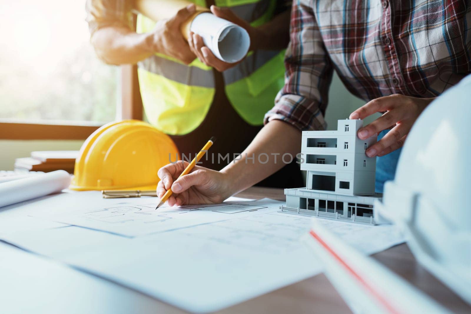 Engineers are consulting the team to design an architectural structure for clients with blueprints and building models to work at office.