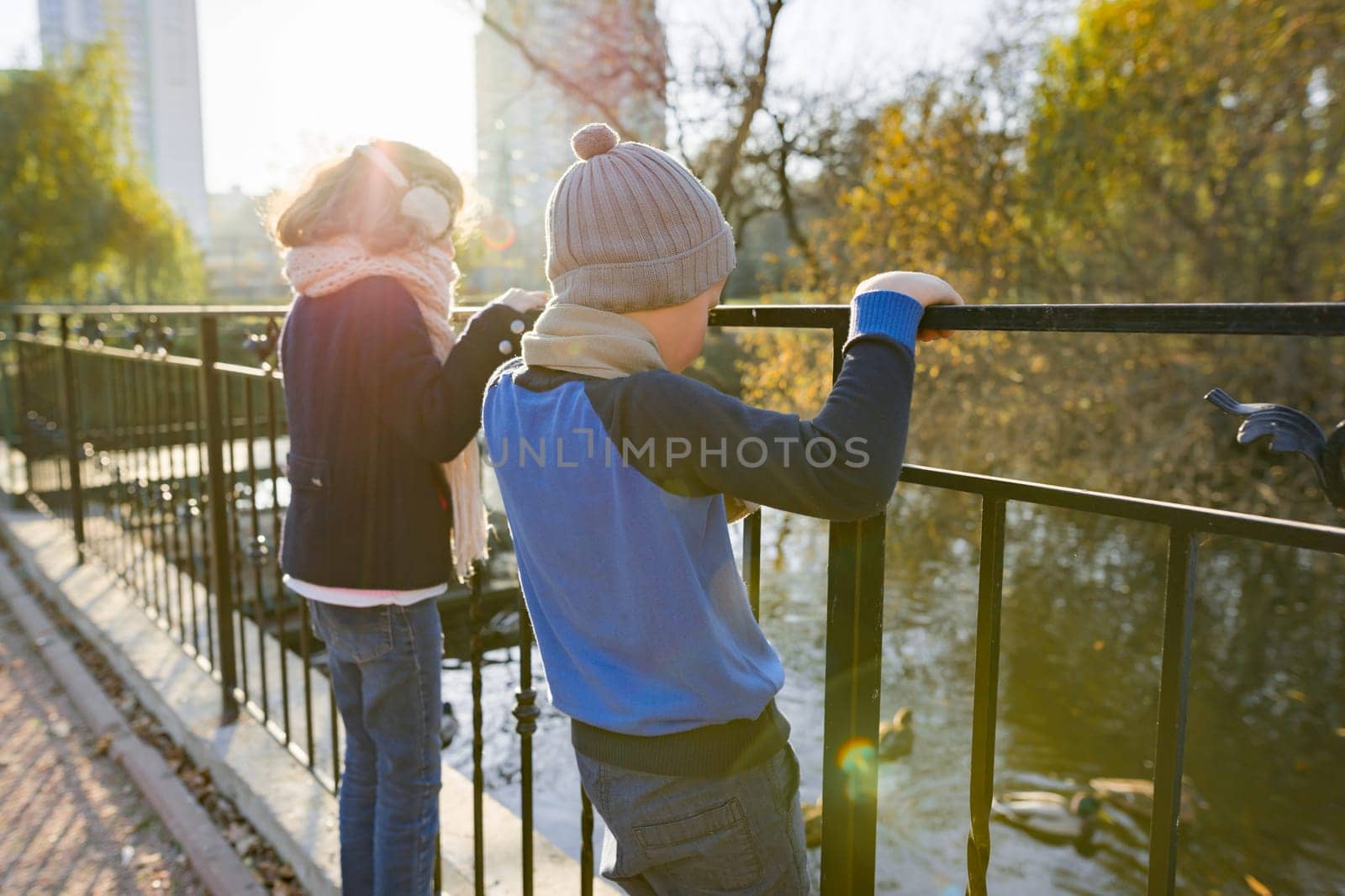 Children boy and girl standing backs on bridge, looking at ducks by VH-studio