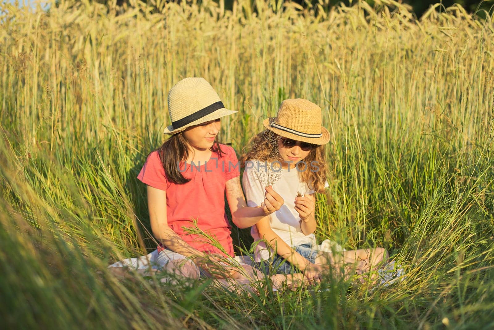 Two smiling girls sitting in grass, children talking by VH-studio