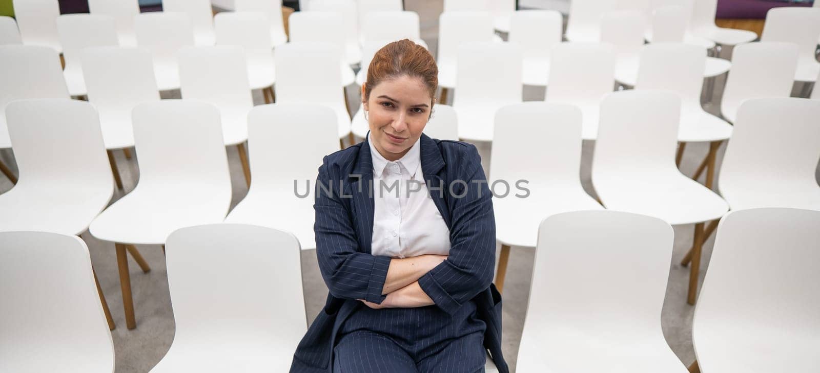 Red-haired caucasian business woman sits on the front row in an empty conference room. by mrwed54