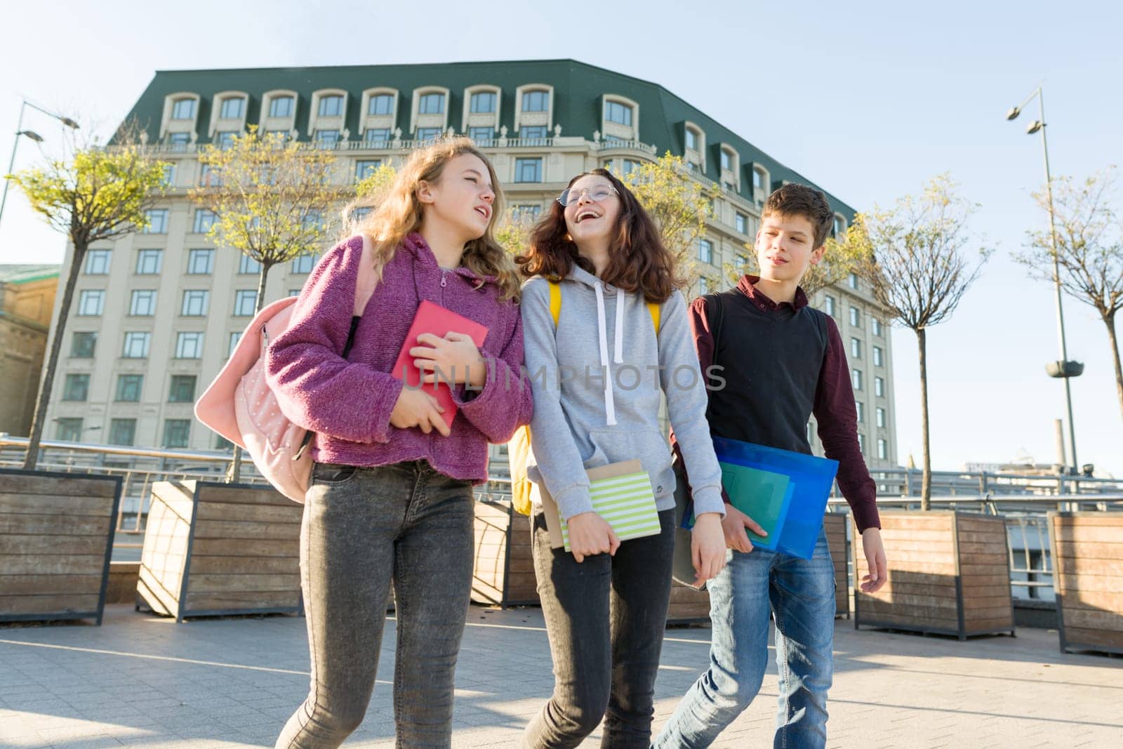 Outdoor portrait of teenage students with backpacks walking and talking. City background, golden hour