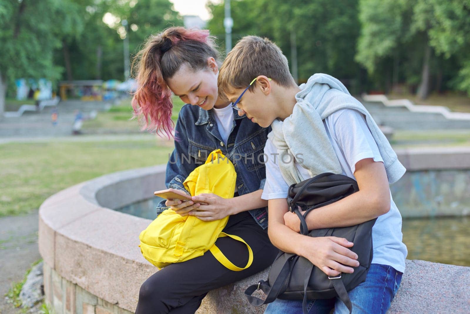 Outdoor portrait of two talking teenagers school students, boy and girl students with smartphone