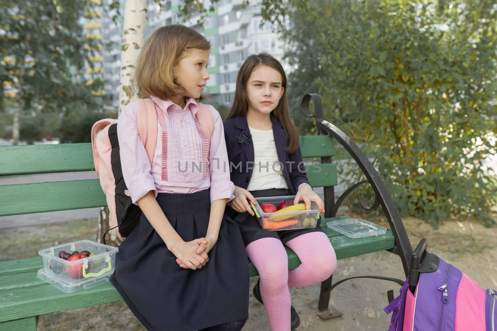 Autumn portrait of children with lunch boxes, school backpacks. Cheerful schoolchildren eat fruit, laughing, talking. Healthy food and healthy lifestyle